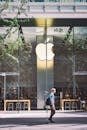 A casual scene of a man walking past the iconic glass facade of an Apple Store in Beijing, China.
